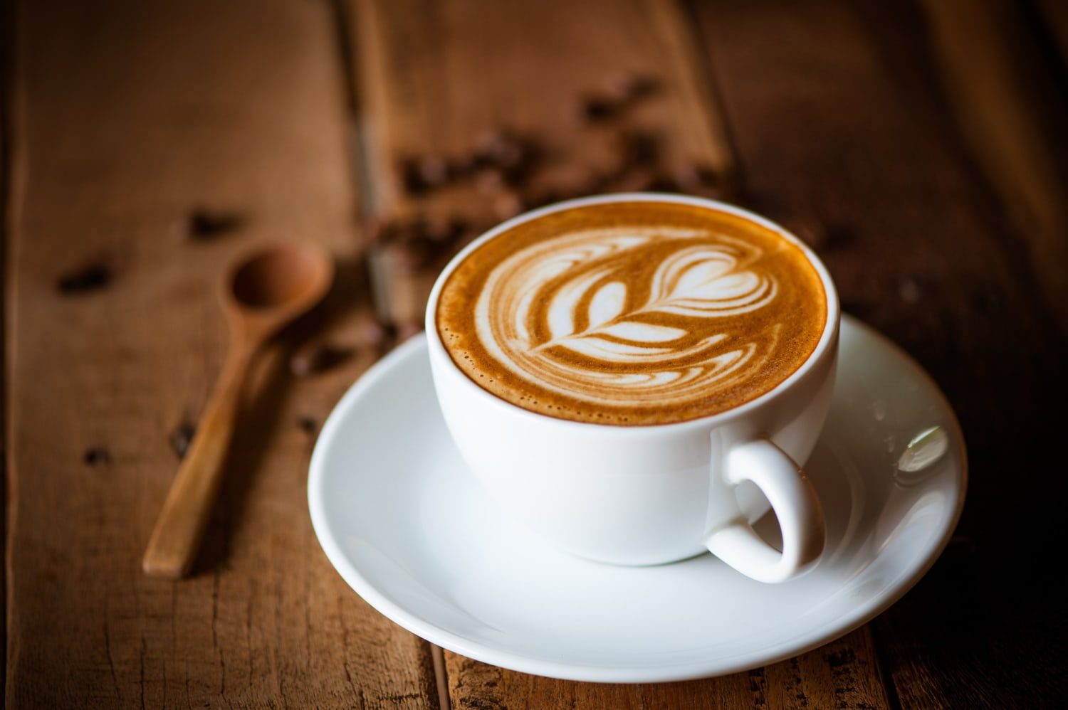 Elegant coffee cup with latte art and coffee beans on rustic wooden table.